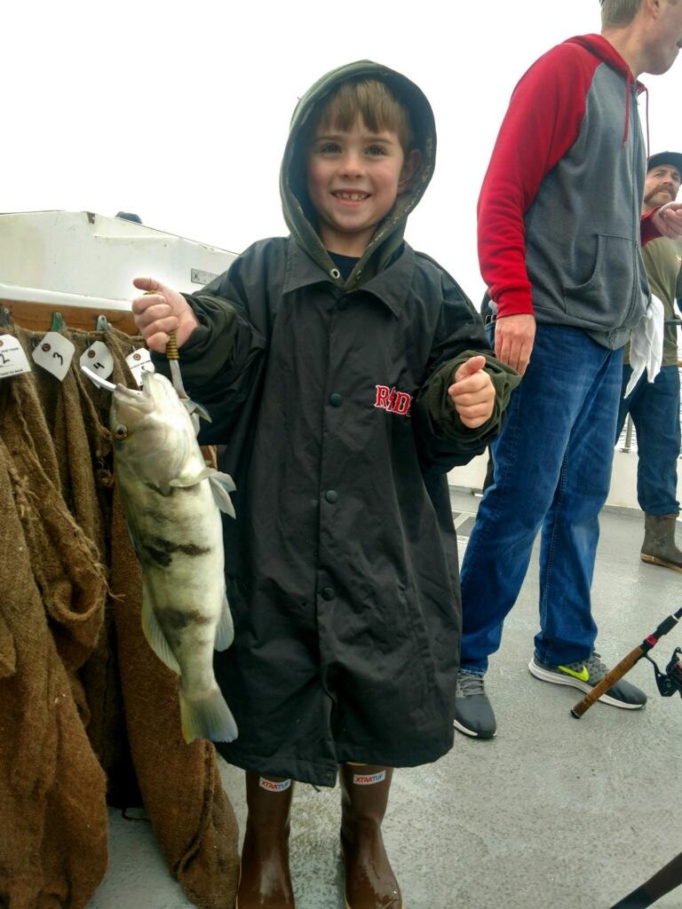 Smiling child in raincoat holding a fish on a boat.