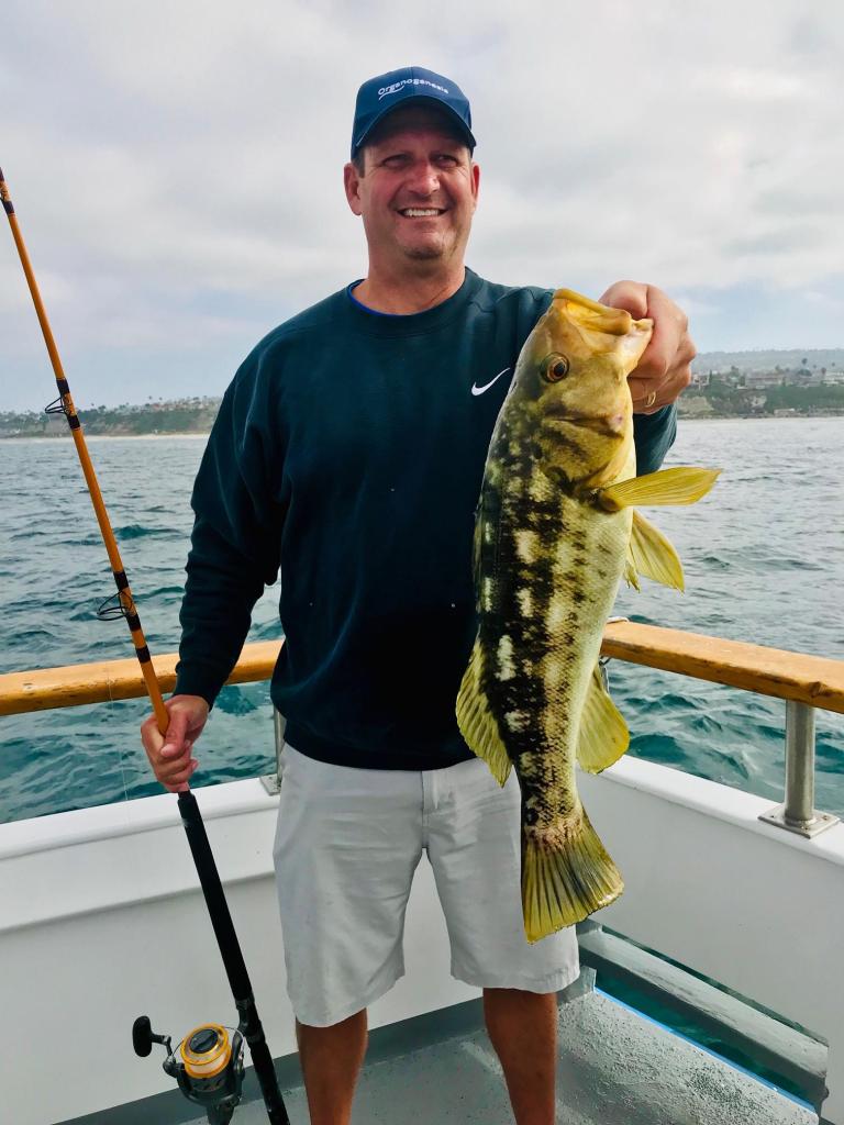 Man on boat holding a large fish with a fishing rod.