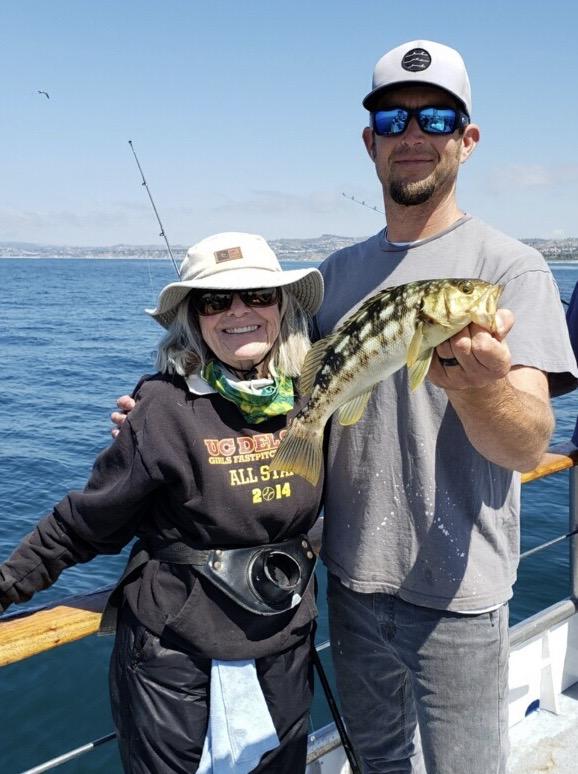 Two people on a boat holding a fish, smiling at the camera.