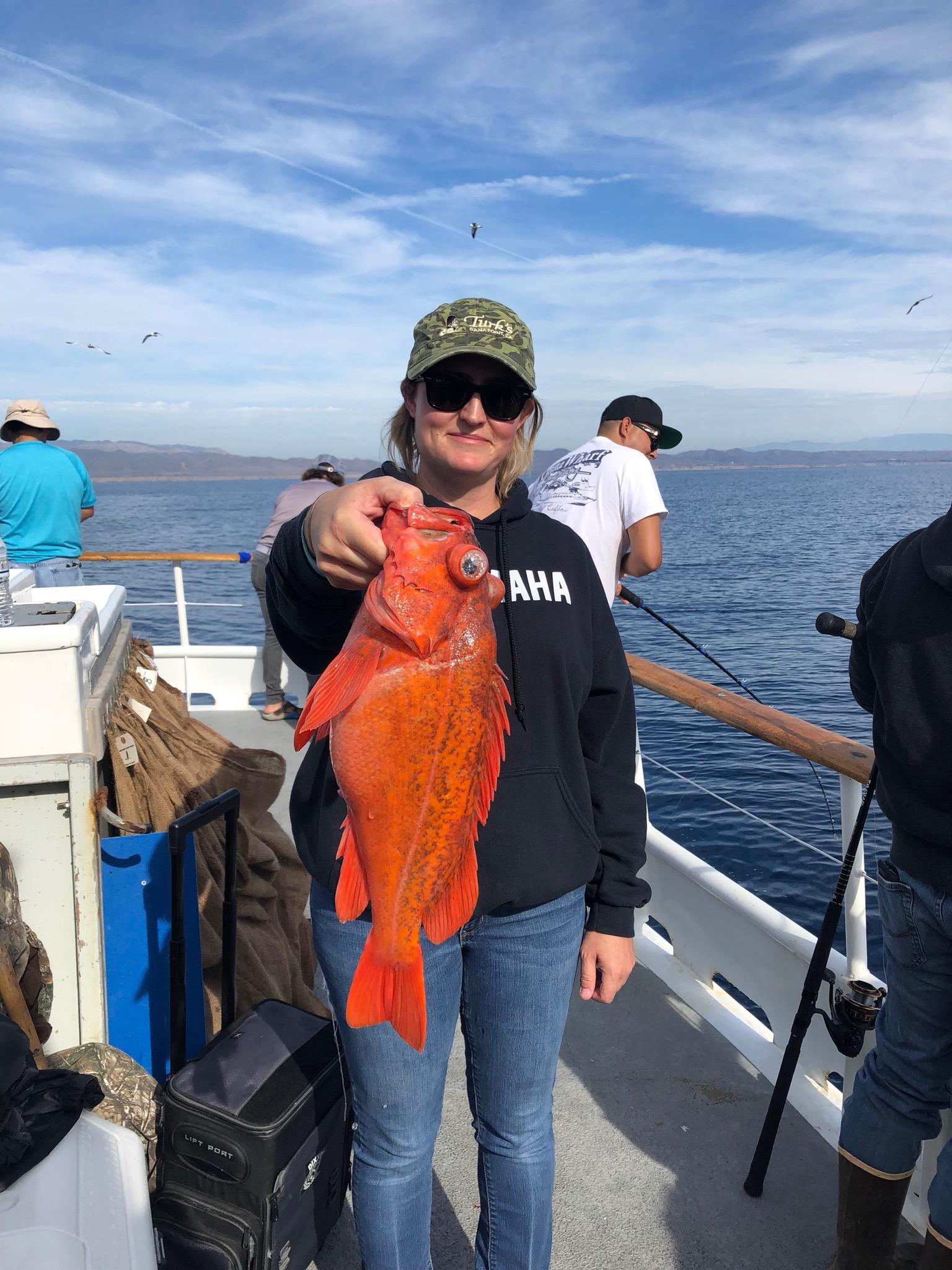 Person holding a large red fish on a boat with others fishing nearby.