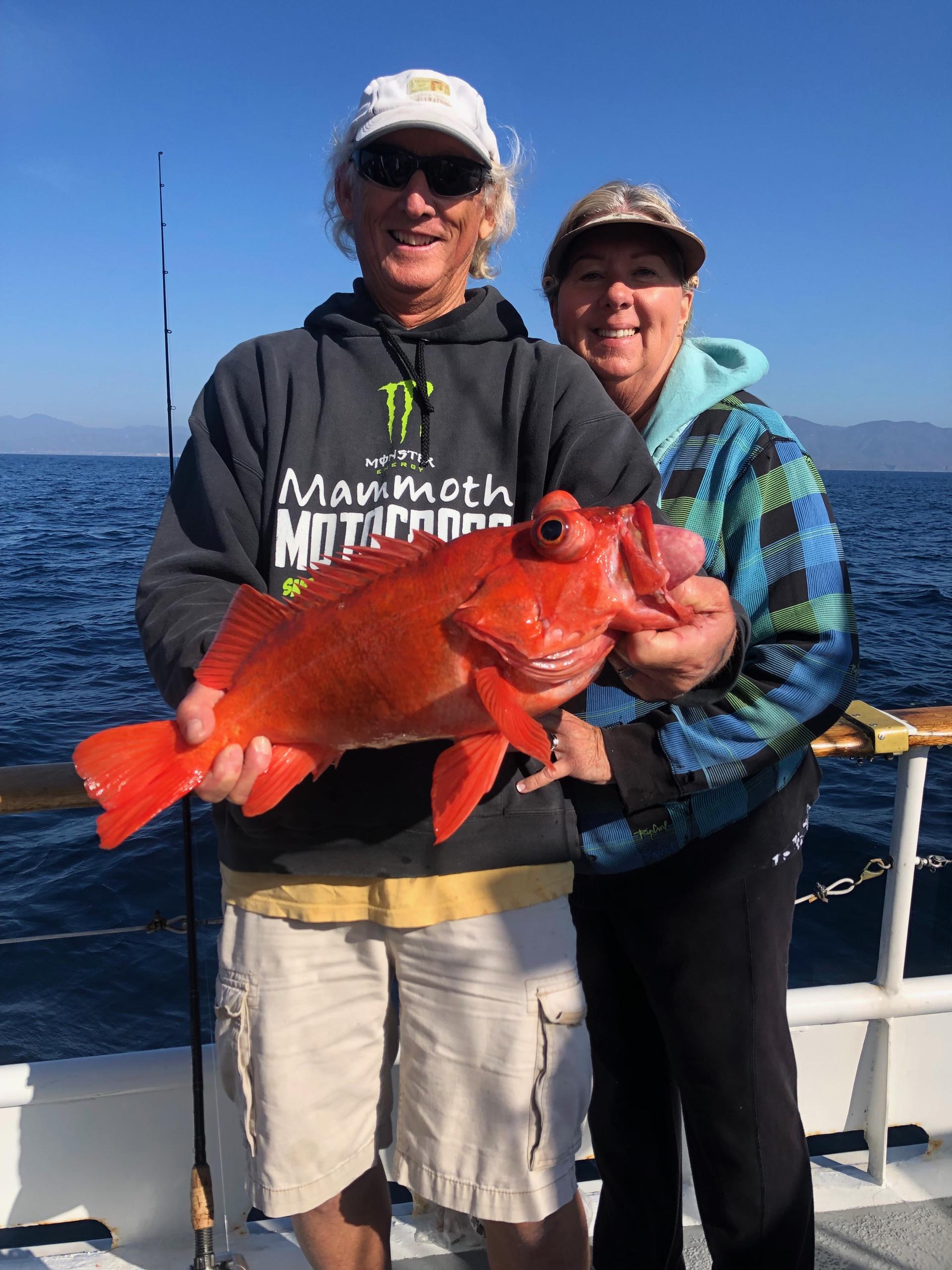 Two people holding a large red fish on a boat with ocean background.
