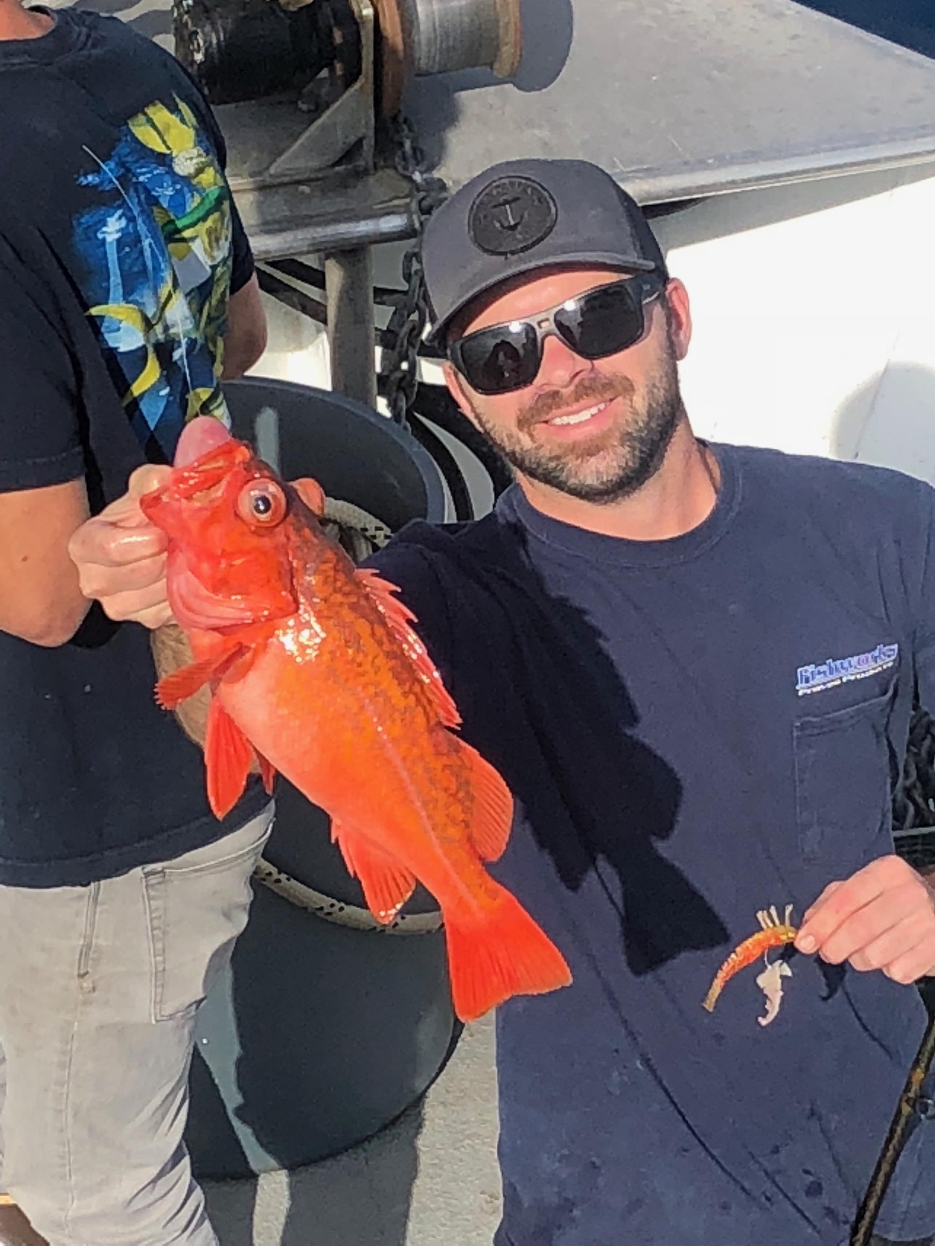 Man in sunglasses holding a bright orange fish on a boat.