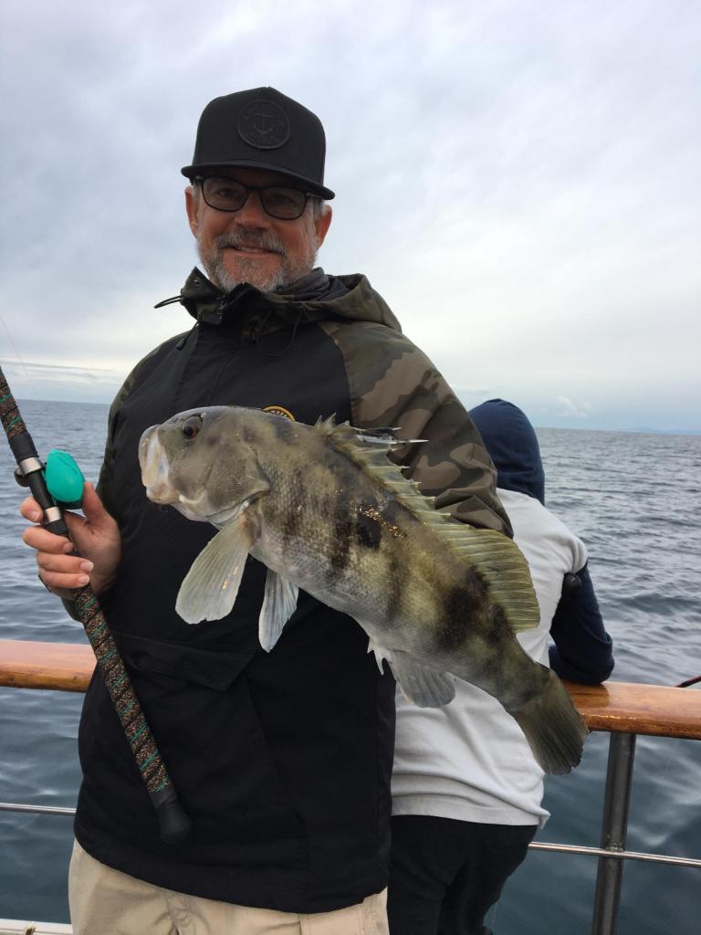 Man holding a large fish on a boat, wearing a jacket and hat.