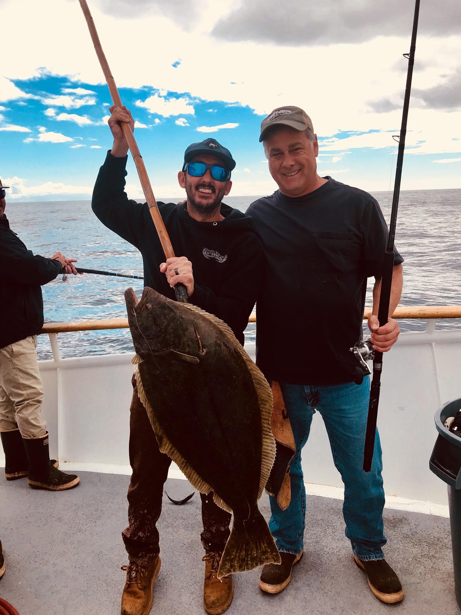 Two men on a boat holding a large fish with fishing rods.