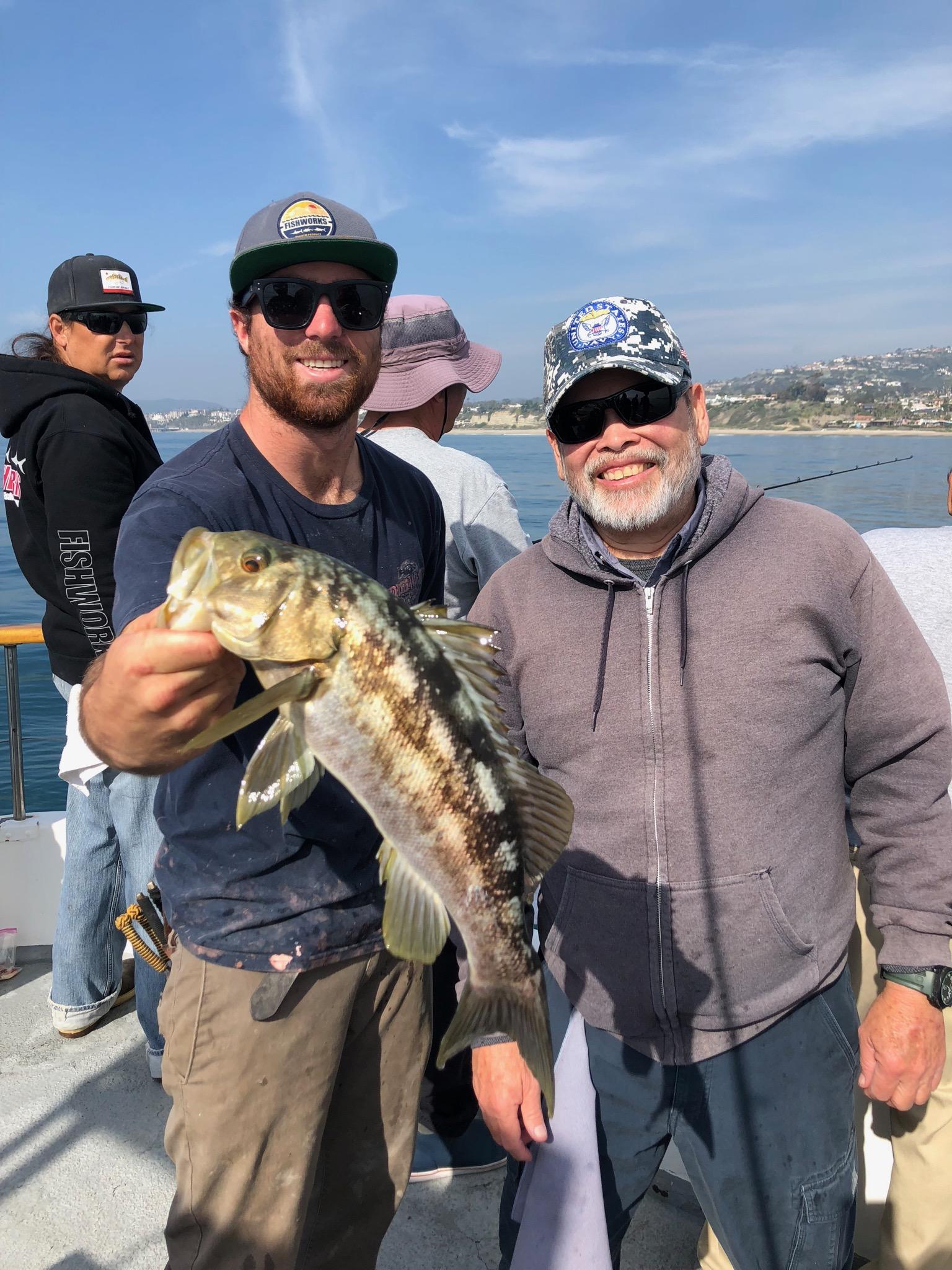 Two men on a boat smiling, one holding a fish.