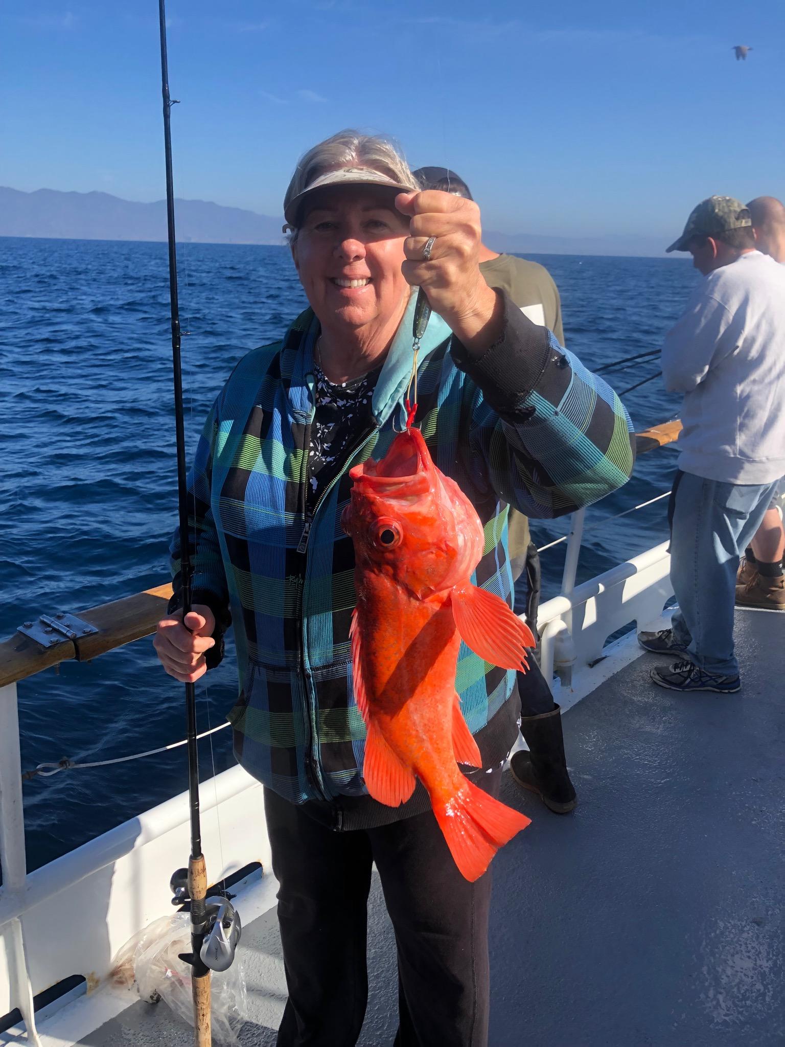 Person holding a large orange fish on a boat with ocean in background.