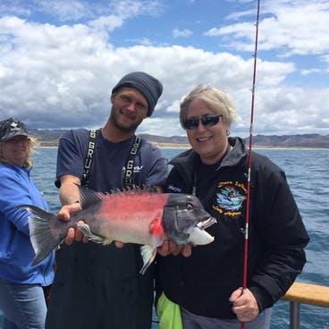 Two people on a boat holding a large red fish with a fishing rod.