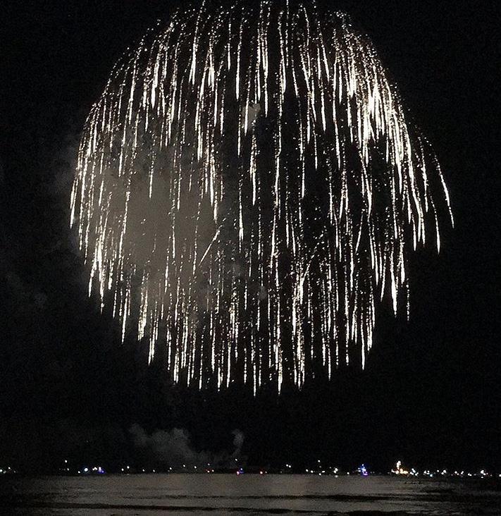 Large firework display over water at night, with reflections on the surface.