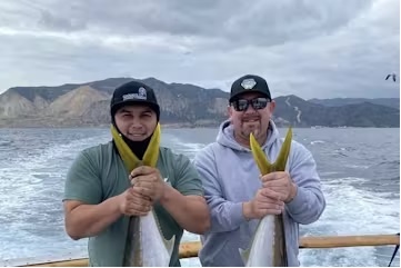 Two people holding fish on a boat with mountains in the background.