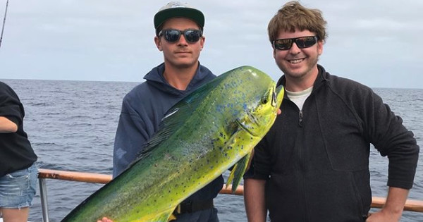 Two people on a boat holding a large yellow-green fish.