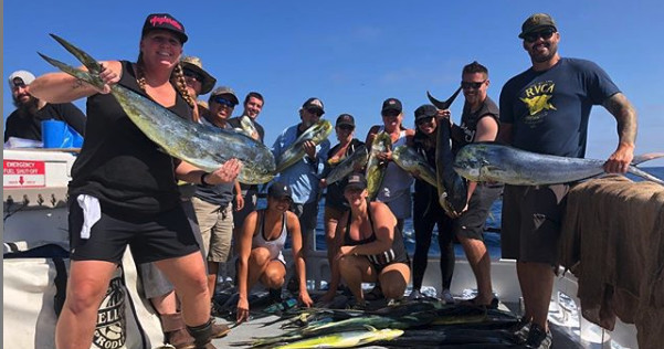 Group of people on a boat holding large fish with a sunny sky.