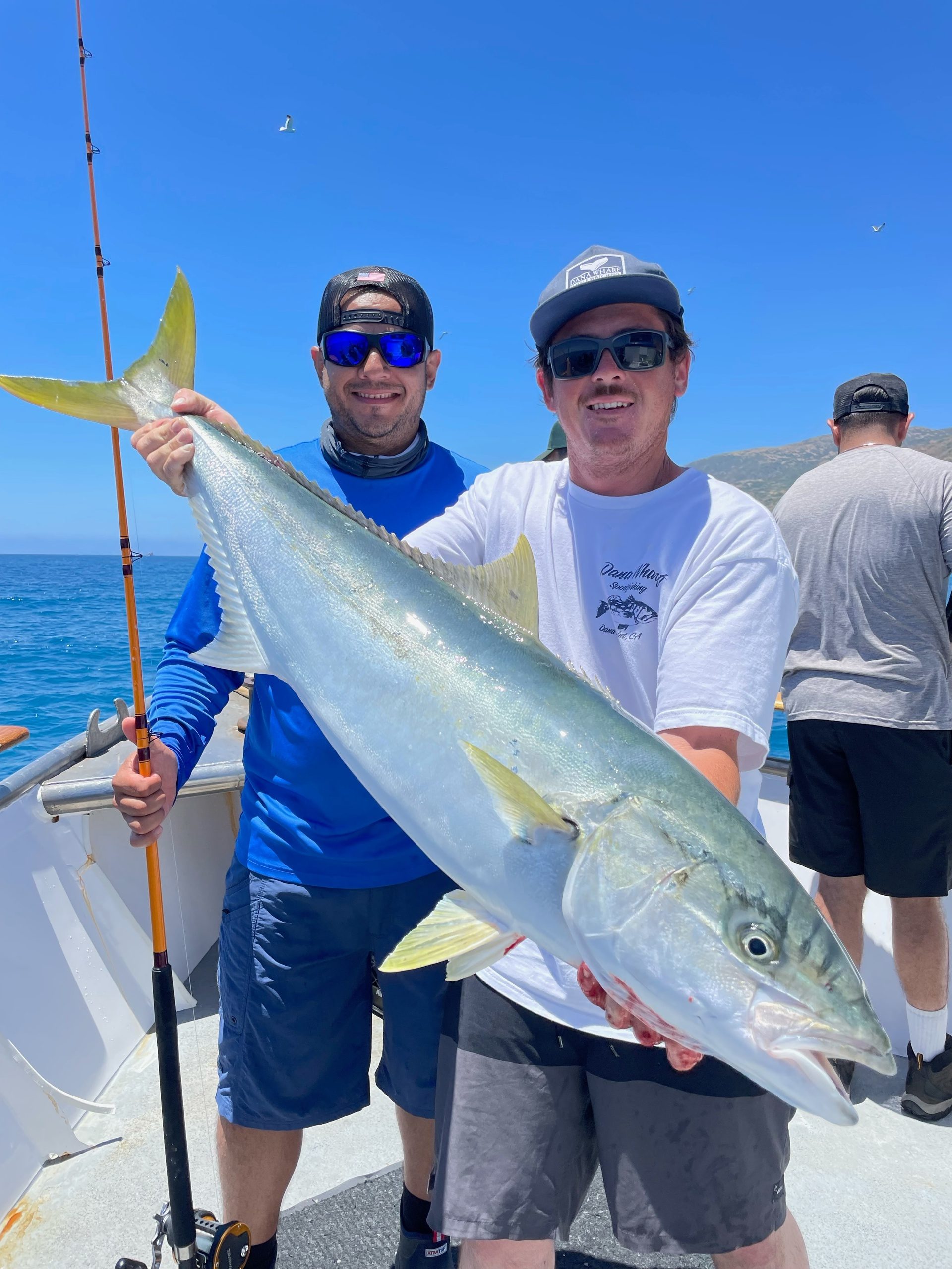 Two men on a boat holding a large yellowtail fish they caught.
