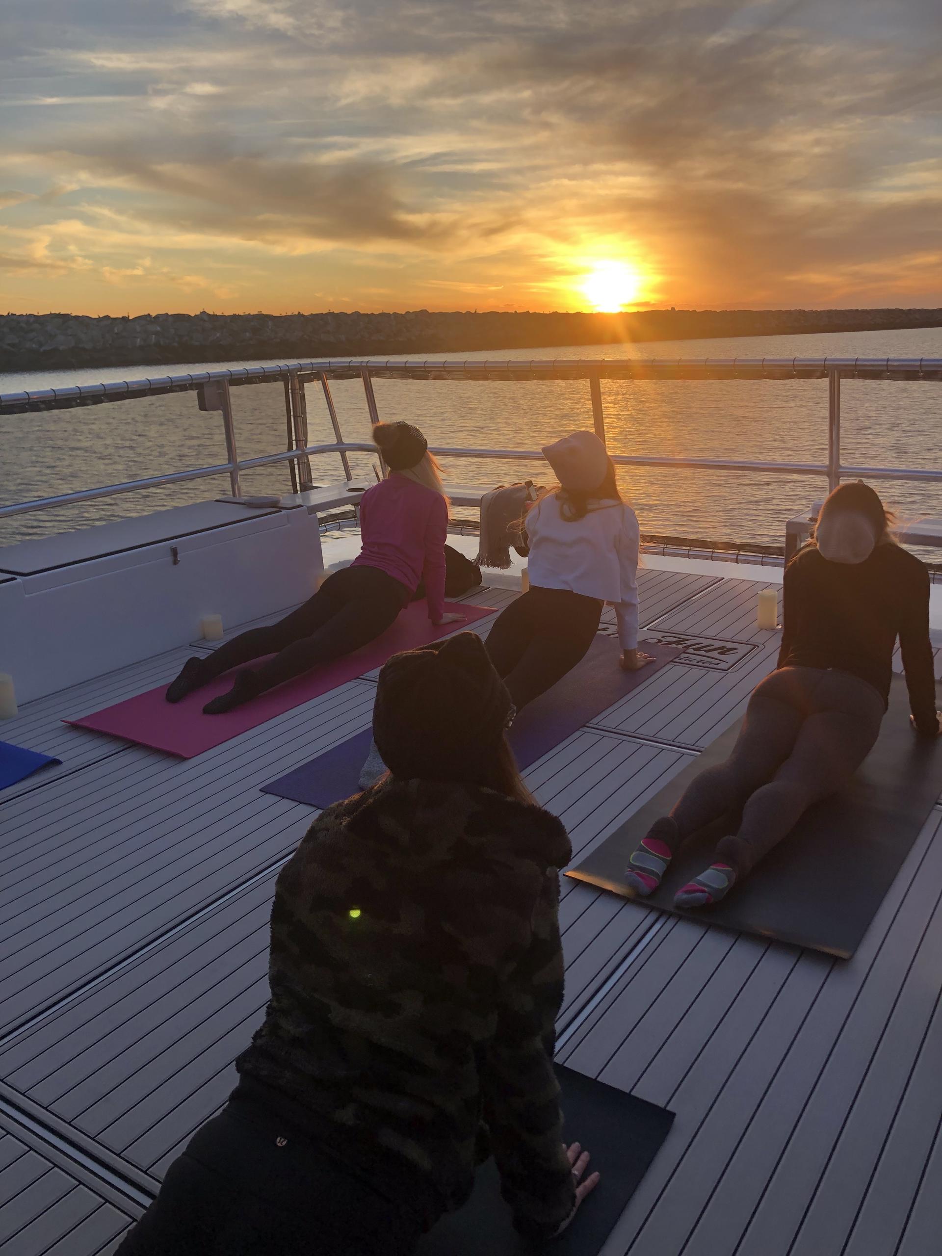 Four people doing yoga on a boat deck at sunset.