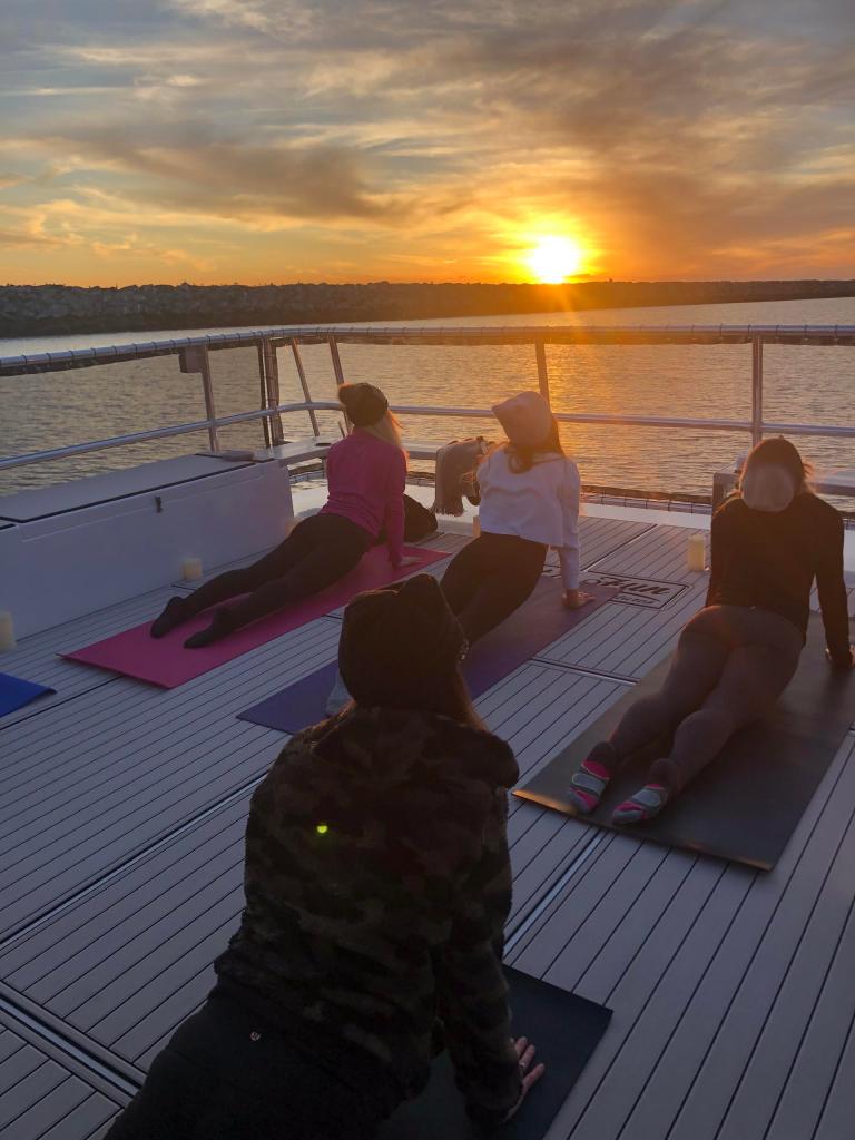 Four people doing yoga on a boat deck at sunset.