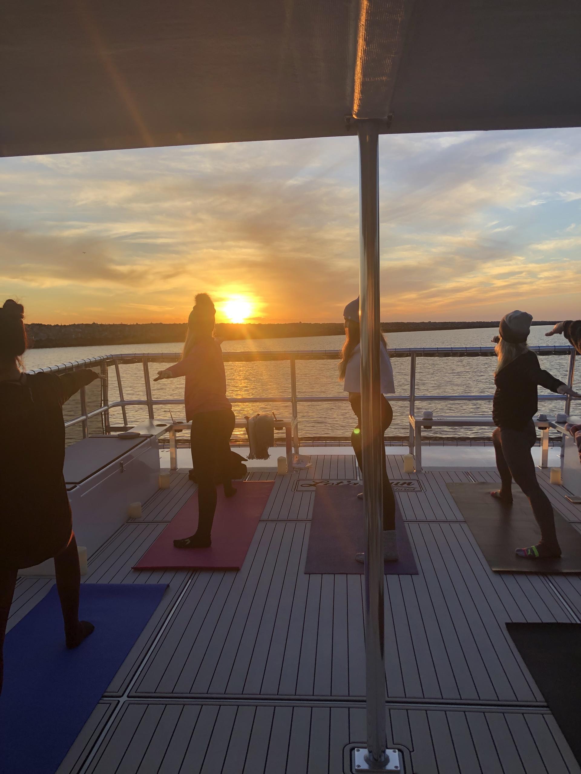 People doing yoga on a boat deck at sunset.