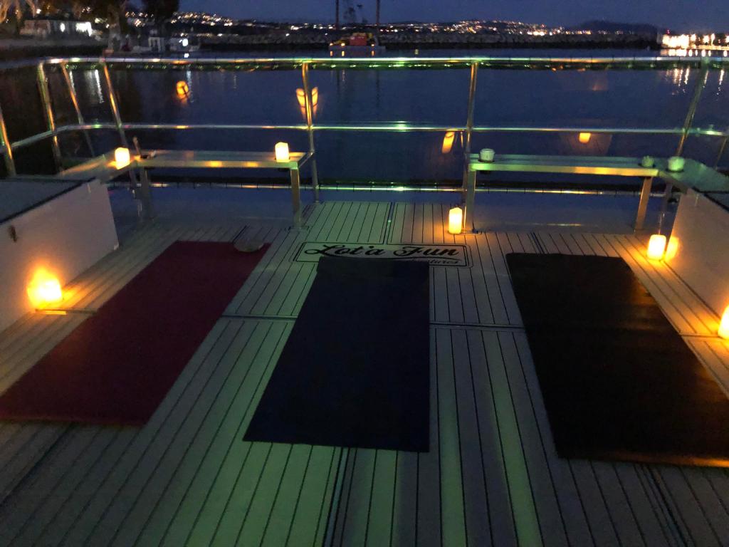 Three yoga mats on a boat deck with ambient lights at dusk.