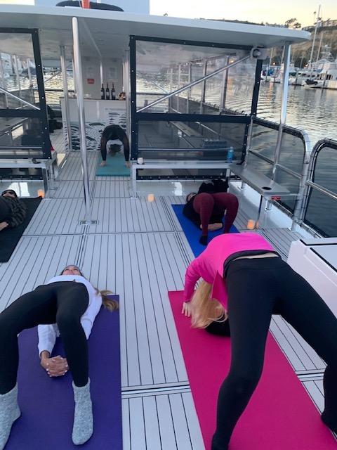 People doing yoga on a boat deck, with a marina in the background.