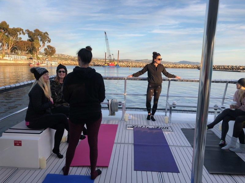 People relaxing on a boat deck with a view of the water and distant cranes.