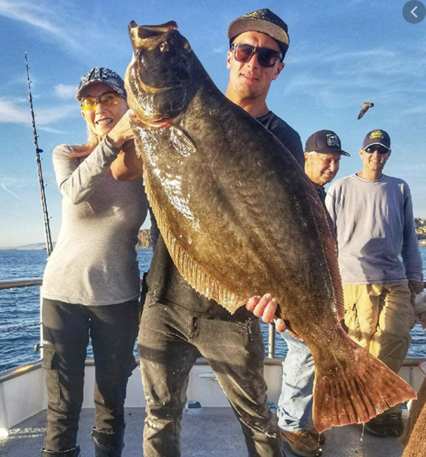 Two people on a boat holding a large fish, with two others in the background.