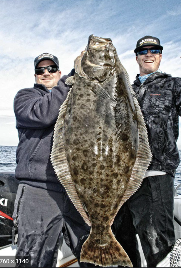 Two men holding a large flat fish on a boat, under a cloudy sky.