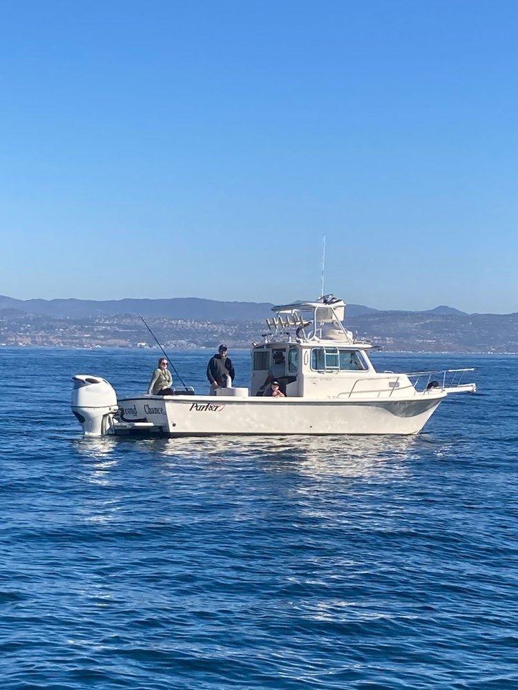 Boat with two people fishing on a calm sea under clear blue sky.