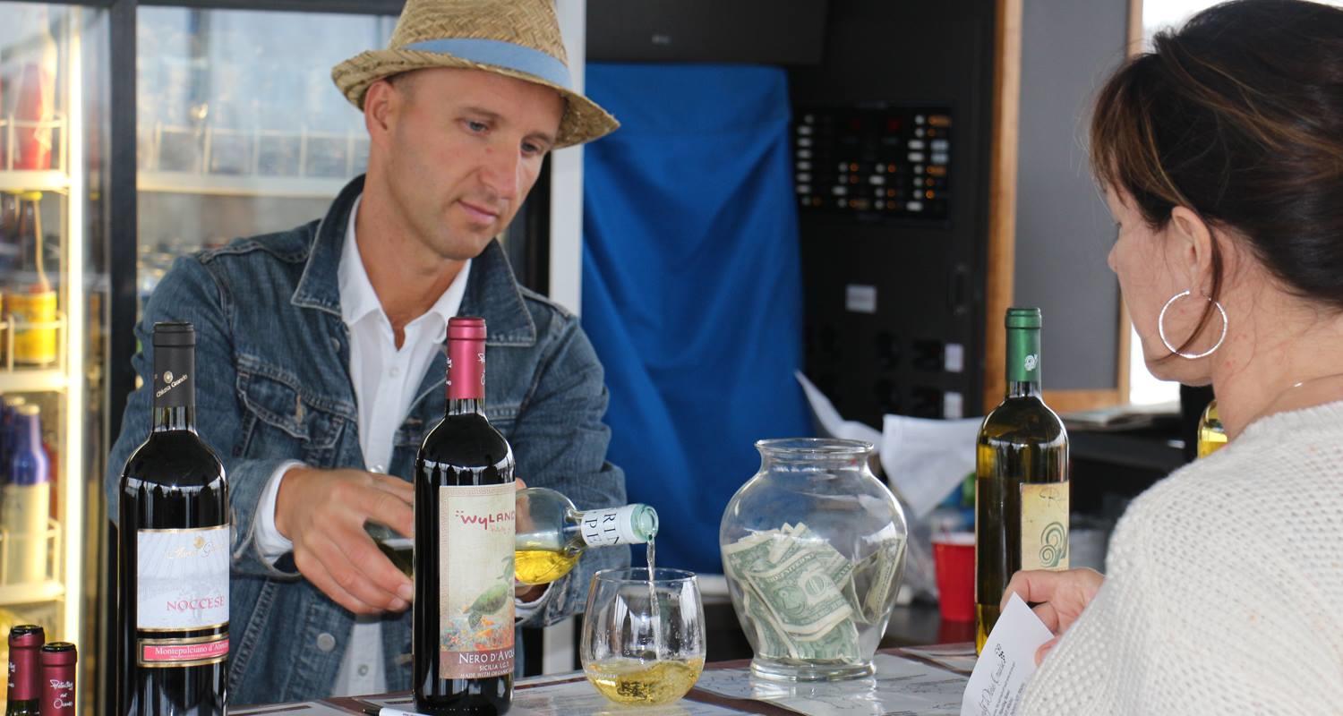 Man in hat pours wine at a bar; woman watches.