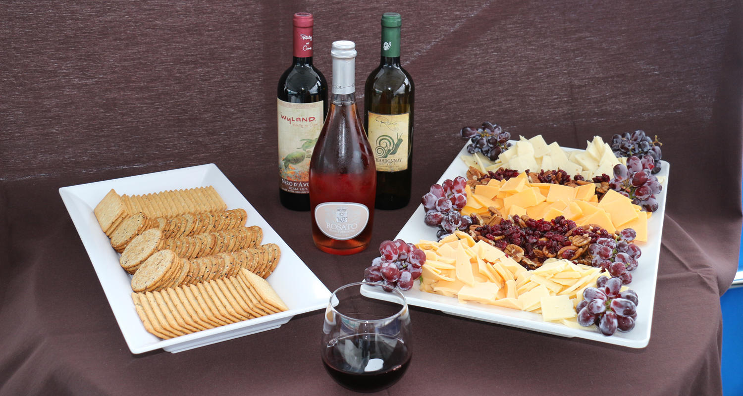Wine bottles with cheese, crackers, grapes on platters.