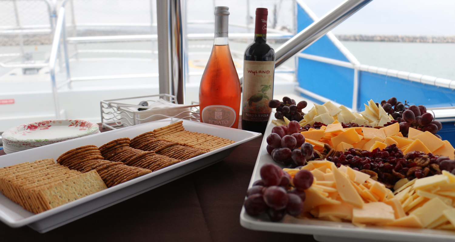 Cheese, grapes, and crackers on trays with wine bottles on a table.