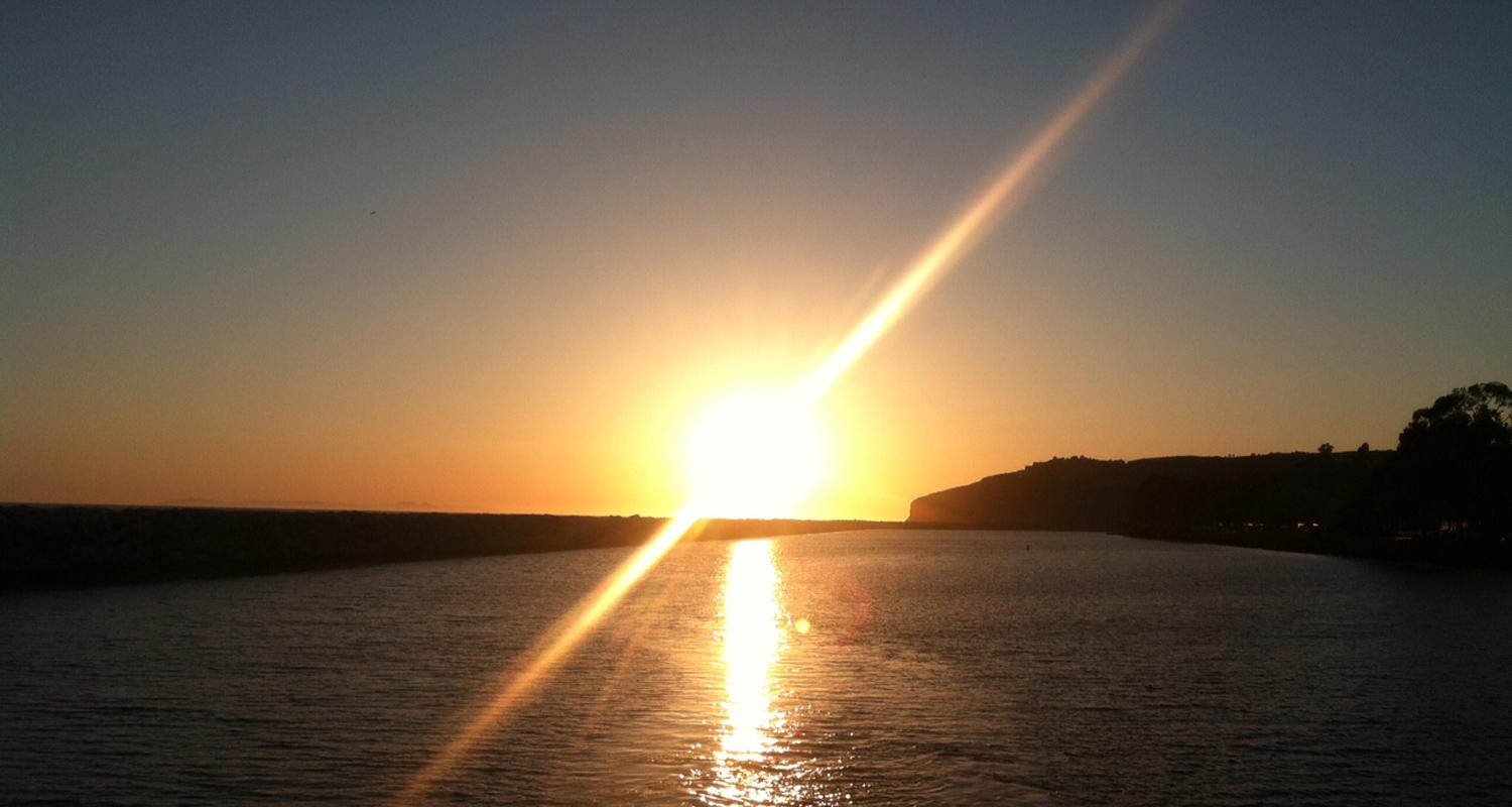 Sunset over water with silhouette of distant land on the horizon.