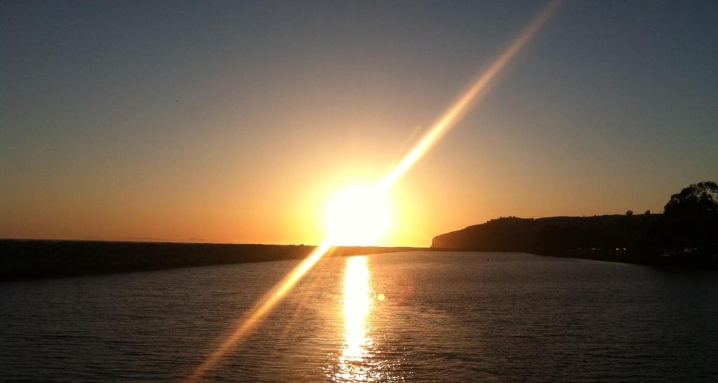 Sunset over water with silhouette of distant land on the horizon.
