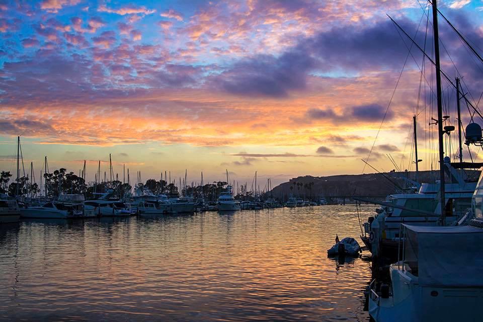 Marina at sunset with boats and colorful sky reflecting on water.