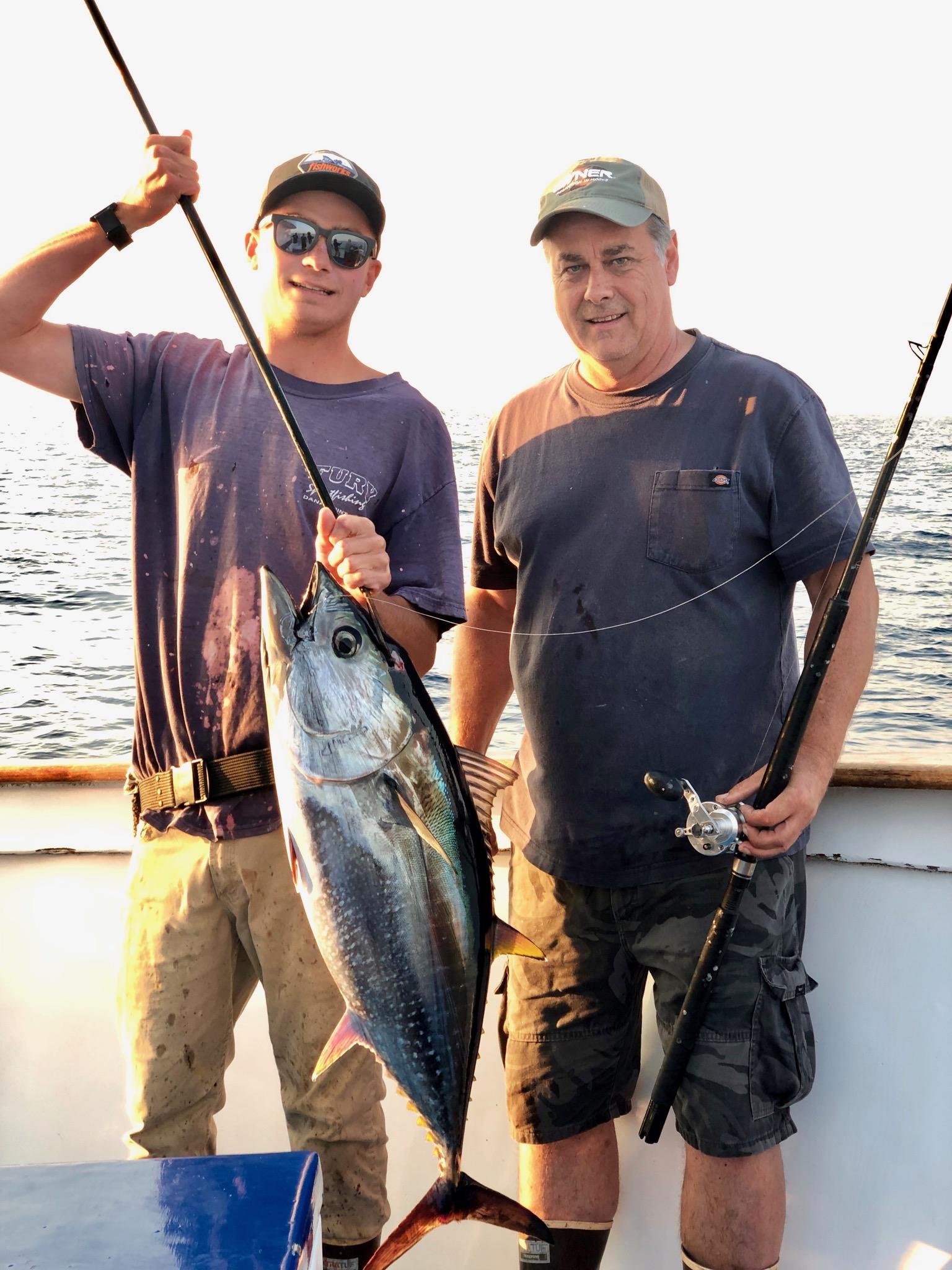 Two men on a boat holding a large fish with fishing rods.
