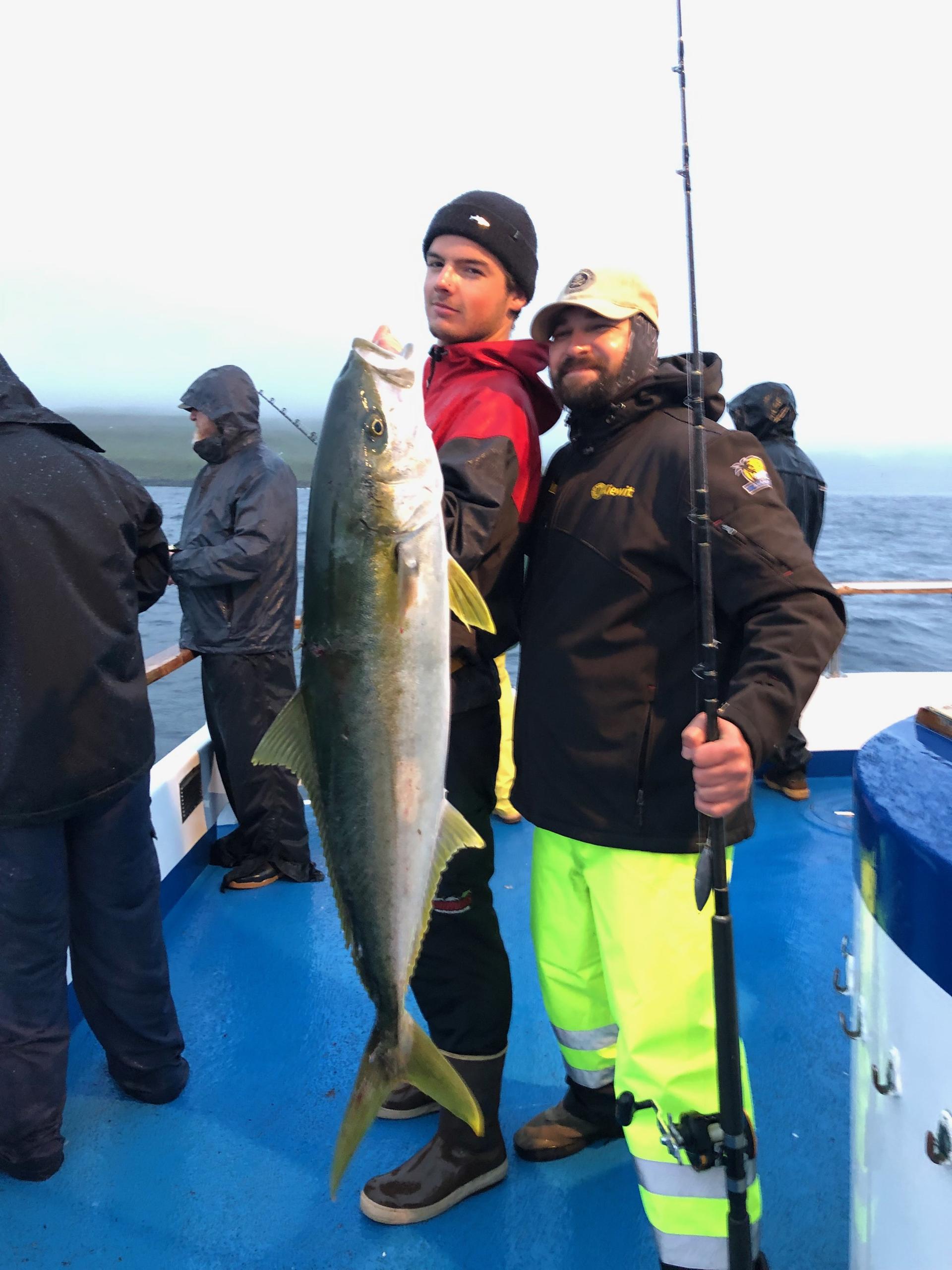 Two people on a boat holding a large fish, others in the background.
