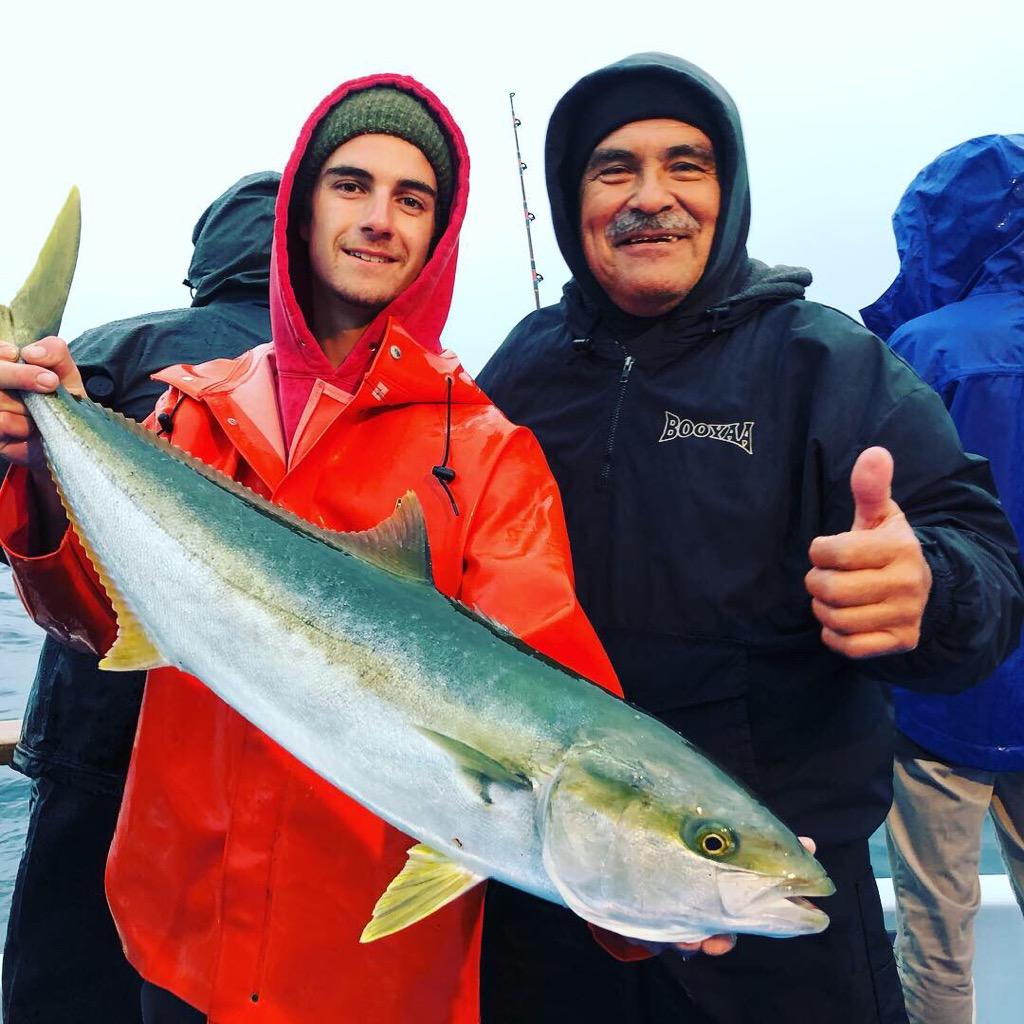 Two people smile and hold a large fish on a boat, other people in the background.