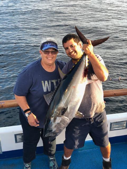 Two people on a boat holding a large fish with the ocean in the background.