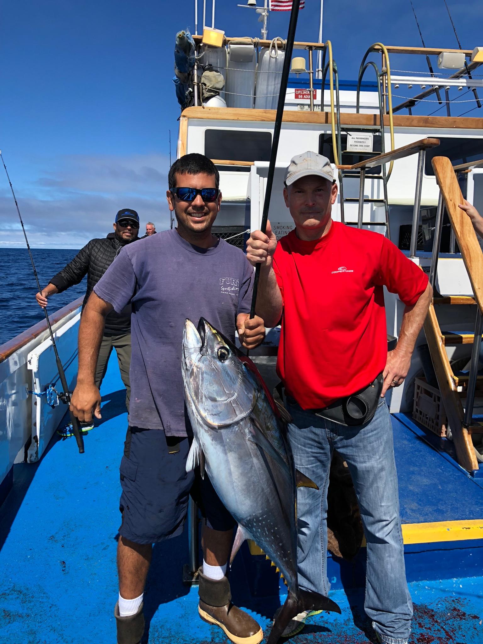 Two men on a boat with a large tuna catch.