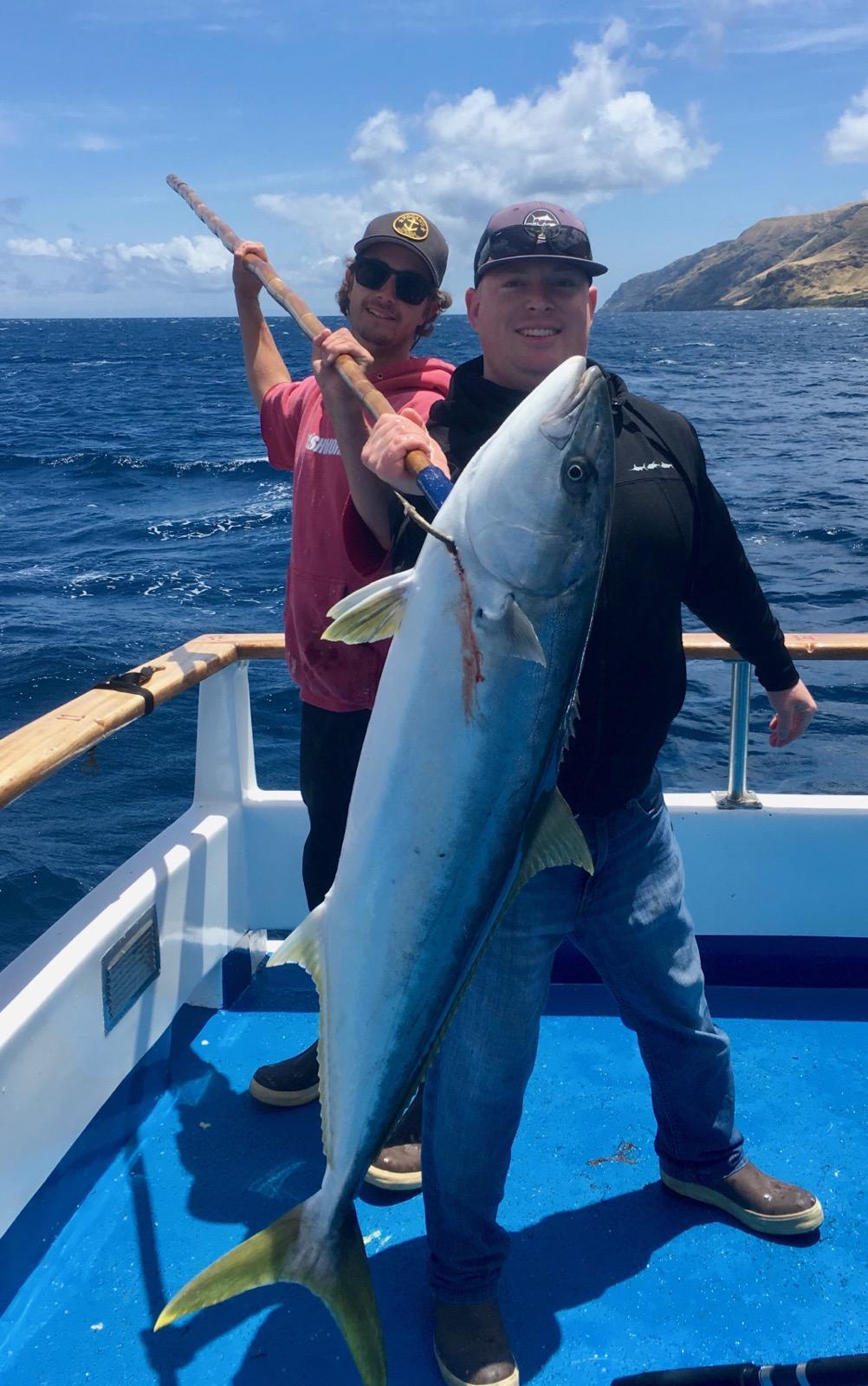 Two people fishing on a boat, holding a large fish against a backdrop of ocean and hills.