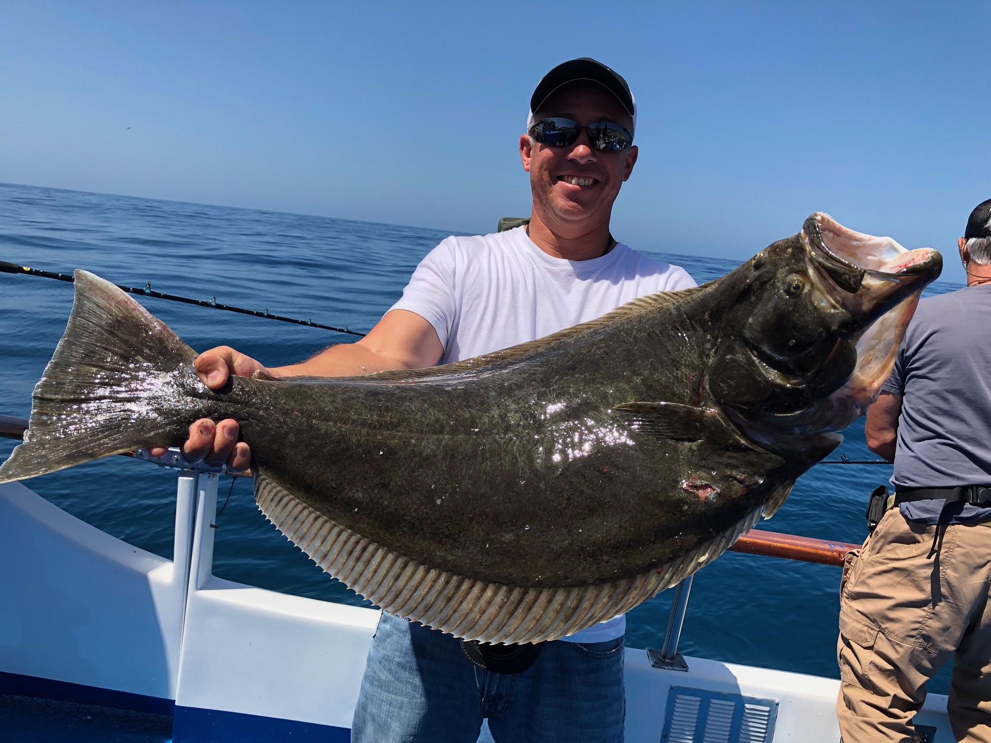 Person on a boat holds a large flat fish with the ocean in the background.
