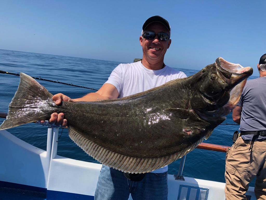 Person on a boat holds a large flat fish with the ocean in the background.