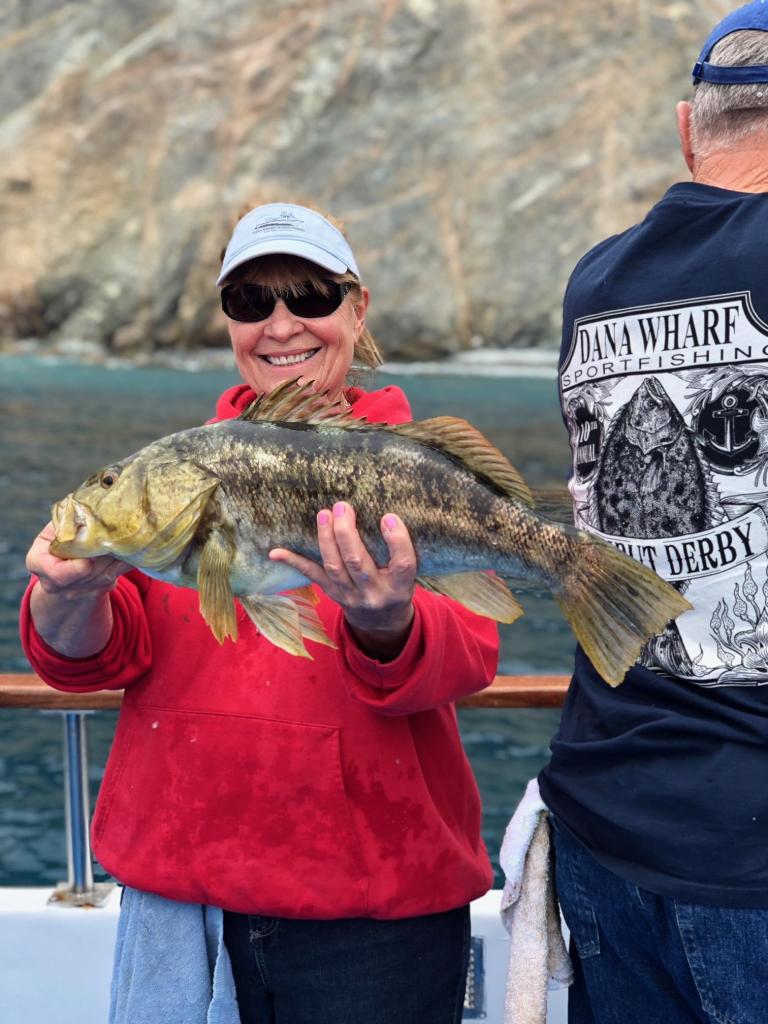 Person in red hoodie happily holding a large fish on a boat.