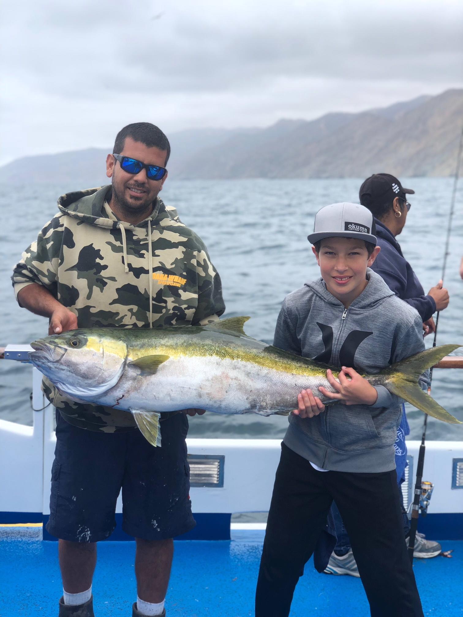 Two people holding a large fish on a boat with the ocean in the background.