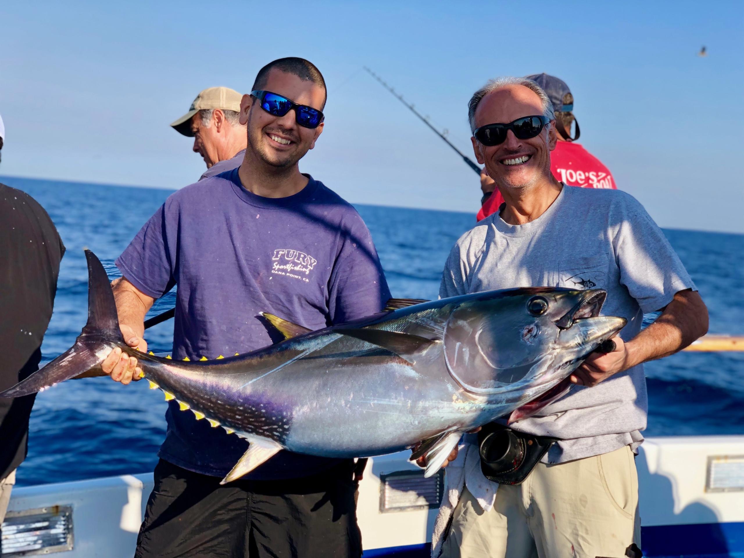 Two men on a boat holding a large tuna fish.