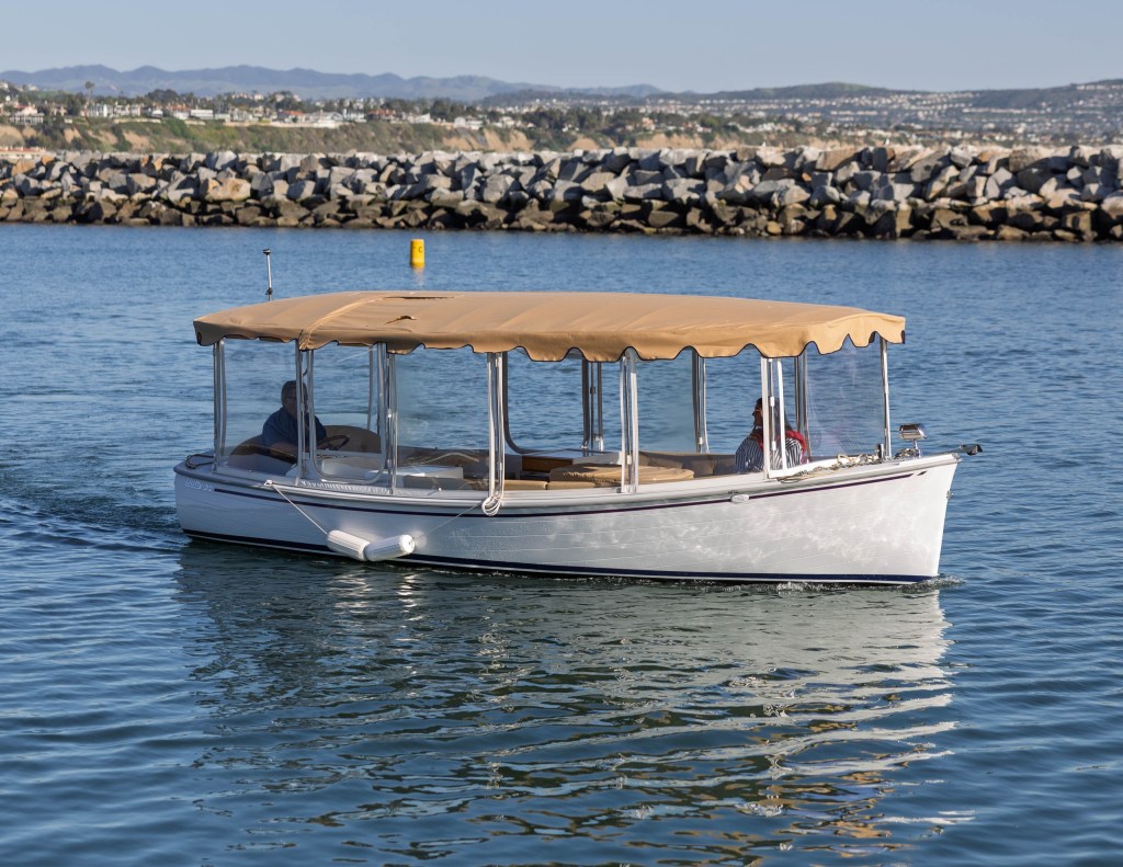 Small covered boat on calm water near rocky shore.