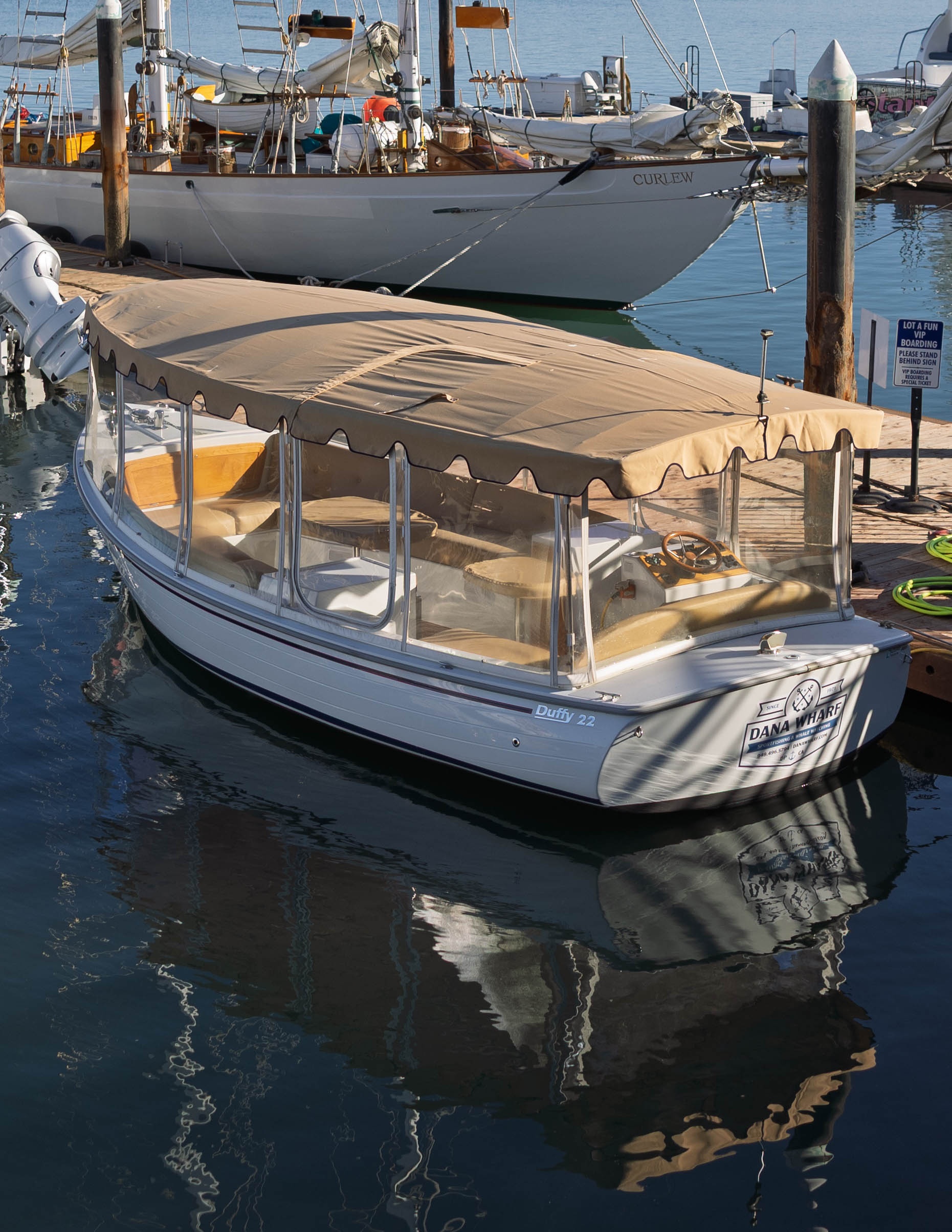 Small covered boat docked in a marina with boats in the background.