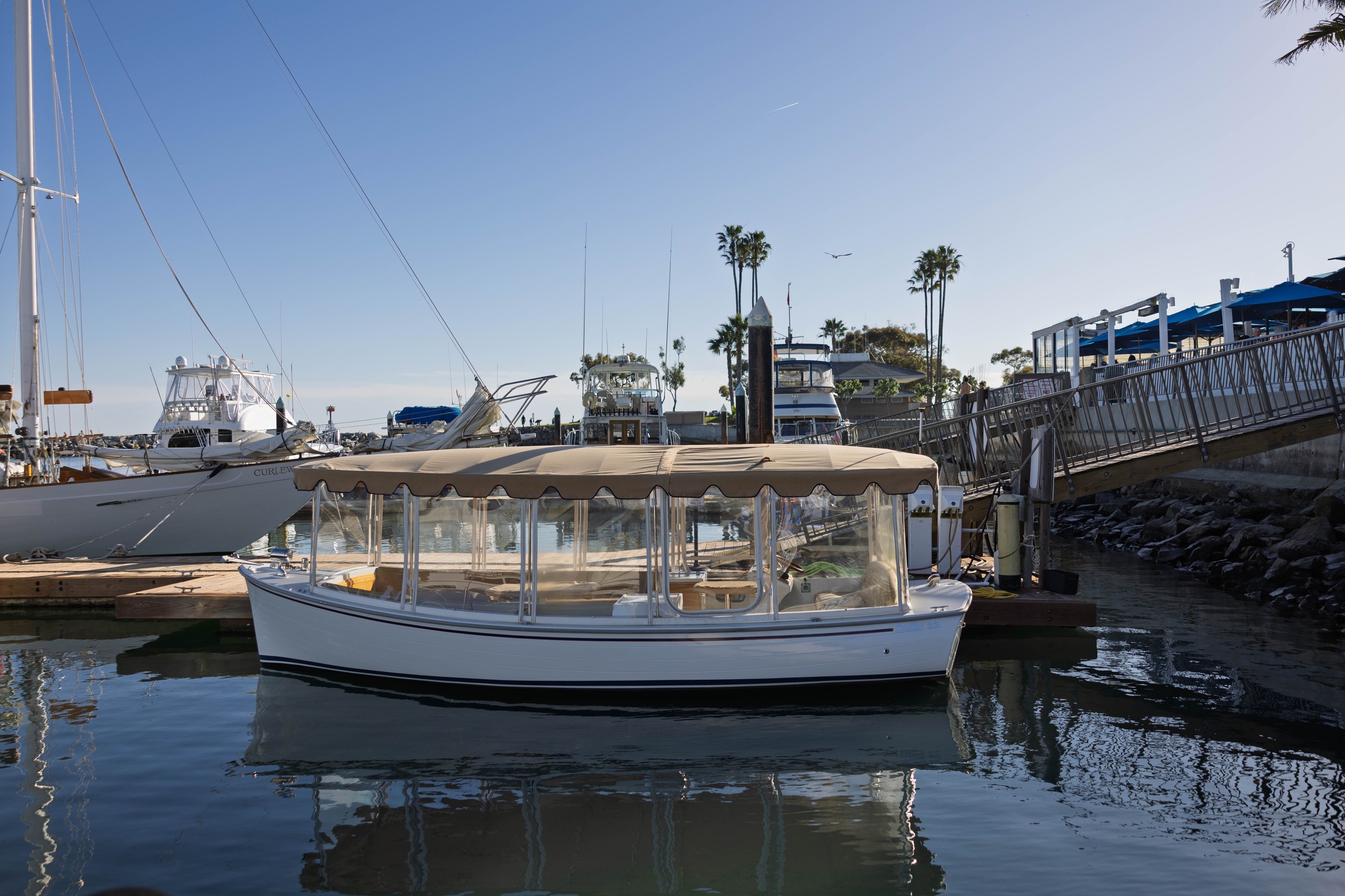 Boat docked in marina with clear sky and palm trees.