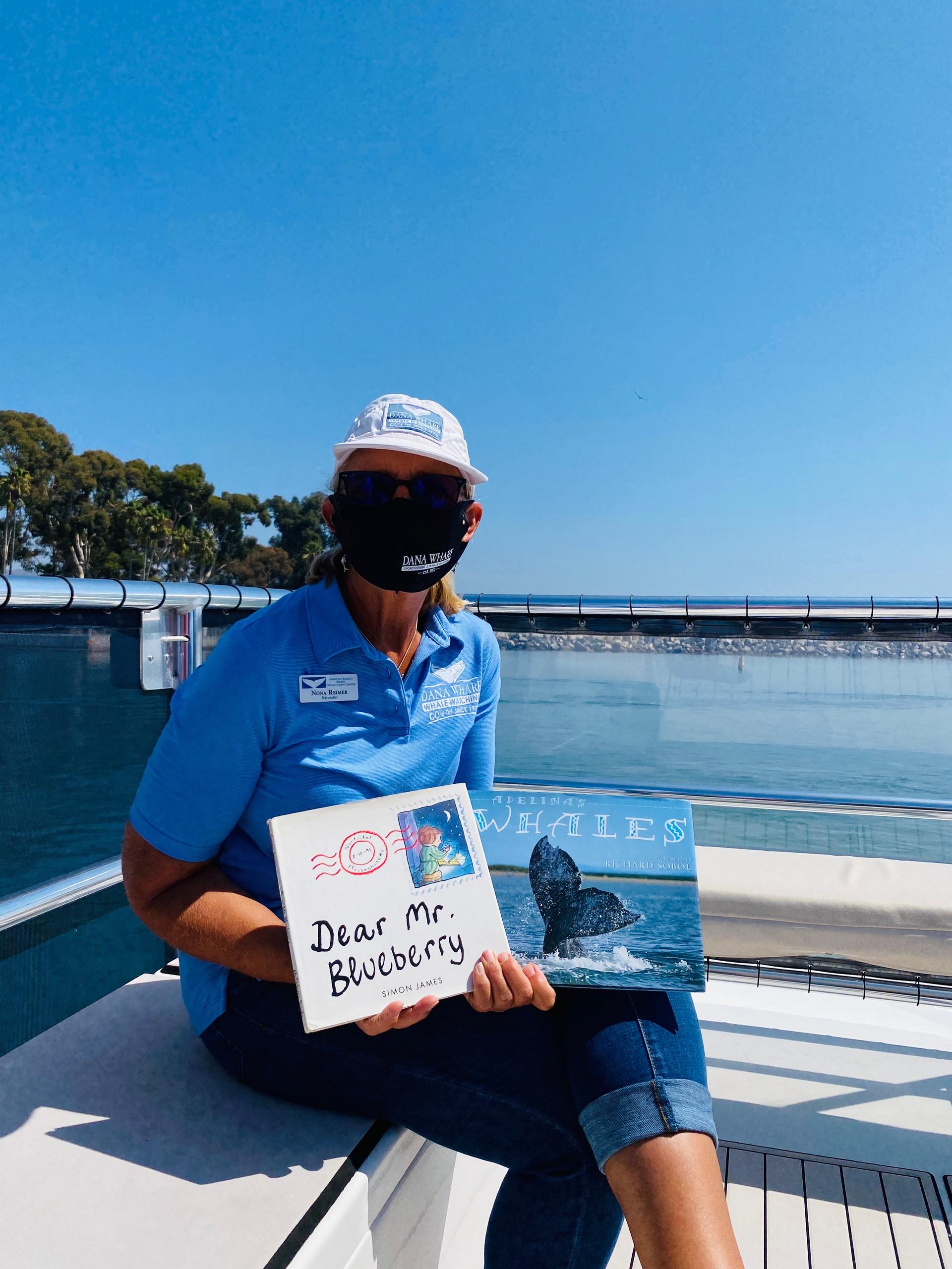 Person in blue shirt and mask holds Dear Mr. Blueberry book on a boat.