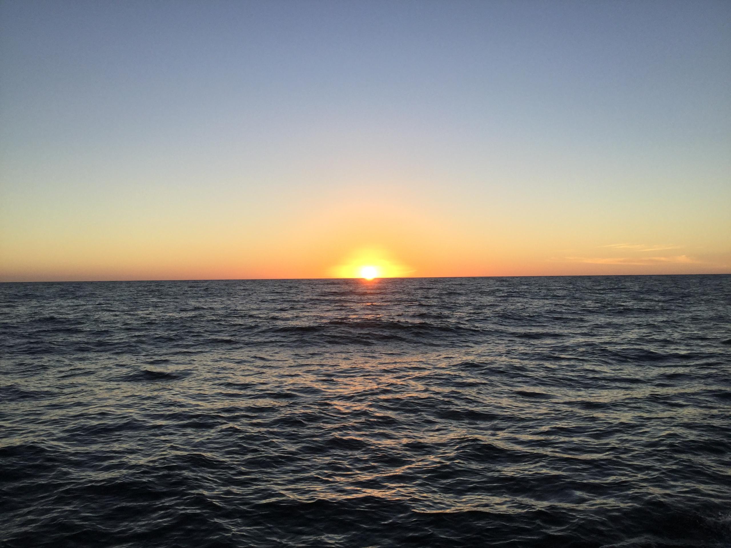 Sunset over a calm ocean with a clear sky.