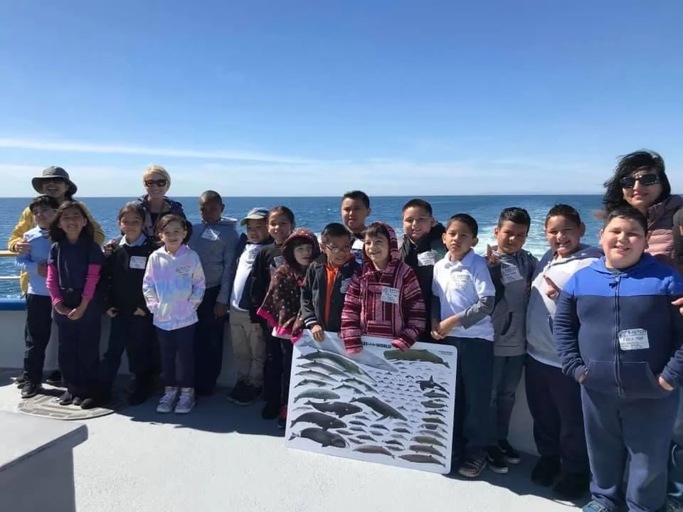 Group of children and adults on a boat holding a fish poster.