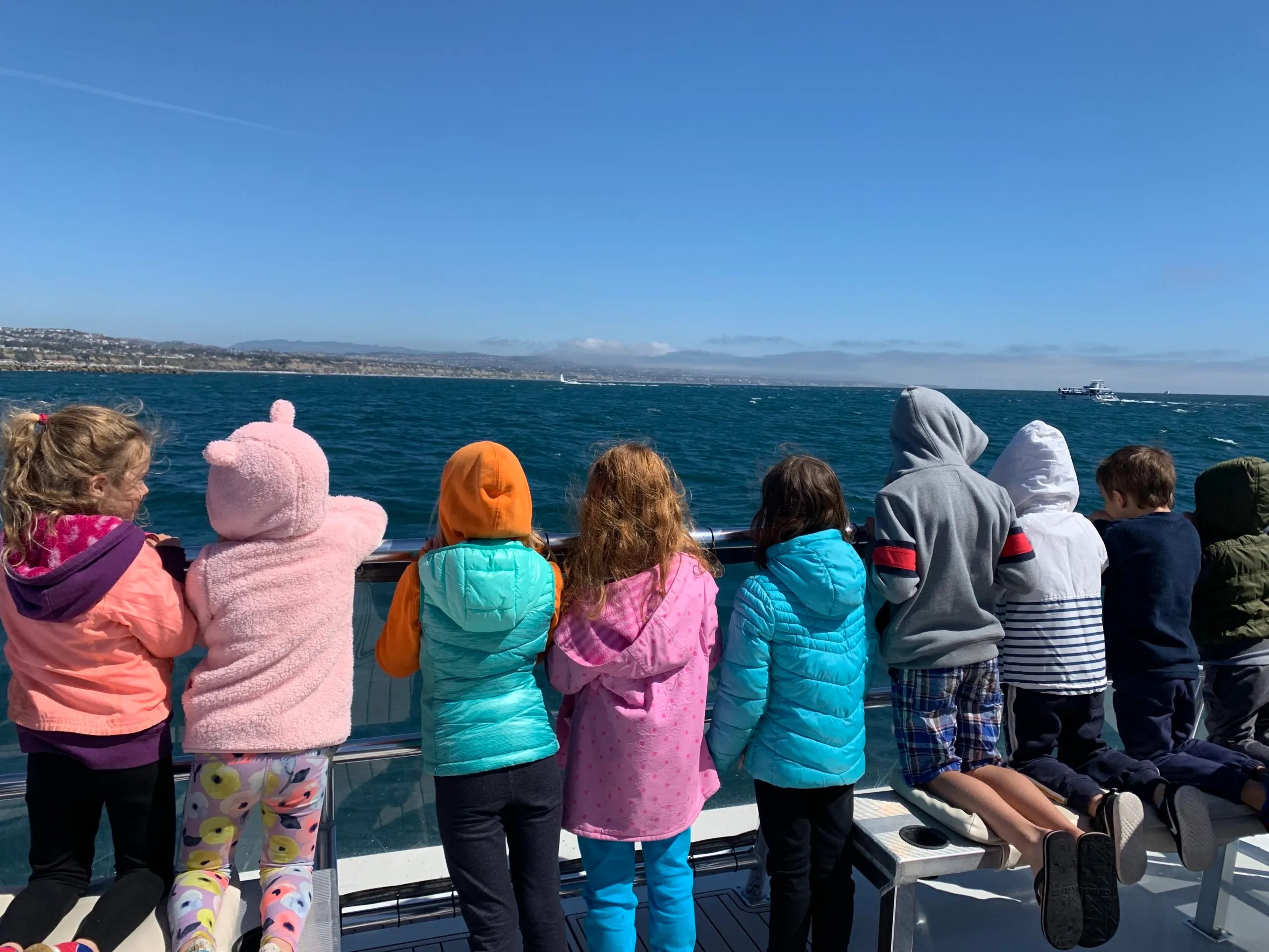 Children in colorful jackets look out to sea from a boat.
