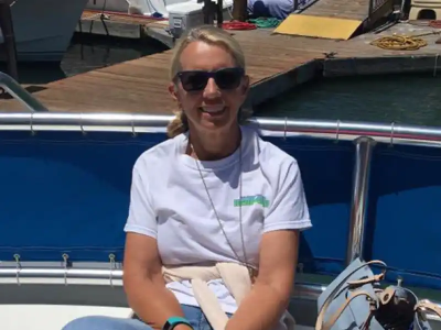 Woman sitting on a boat wearing sunglasses and a white shirt.